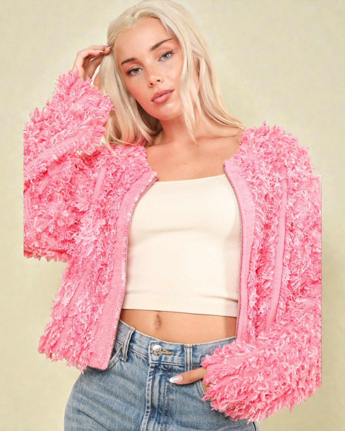 Woman wearing a pink fluffy cardigan over a white top and blue jeans on a beige background