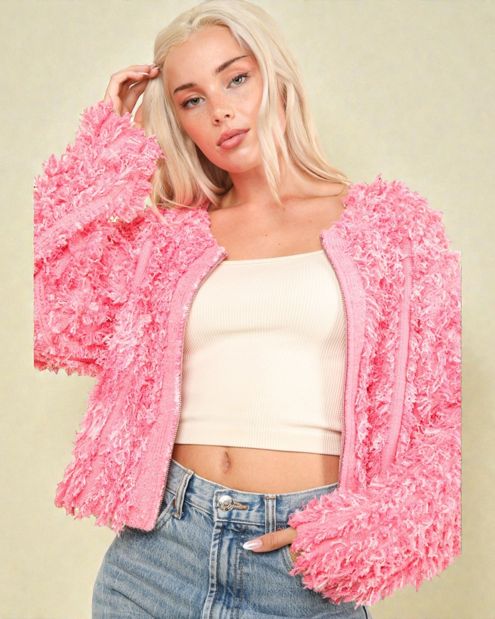 Woman wearing a pink fluffy cardigan over a white top and blue jeans on a beige background