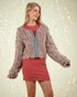 Woman wearing a colorful knitted cardigan over a red top and skirt against a light background.