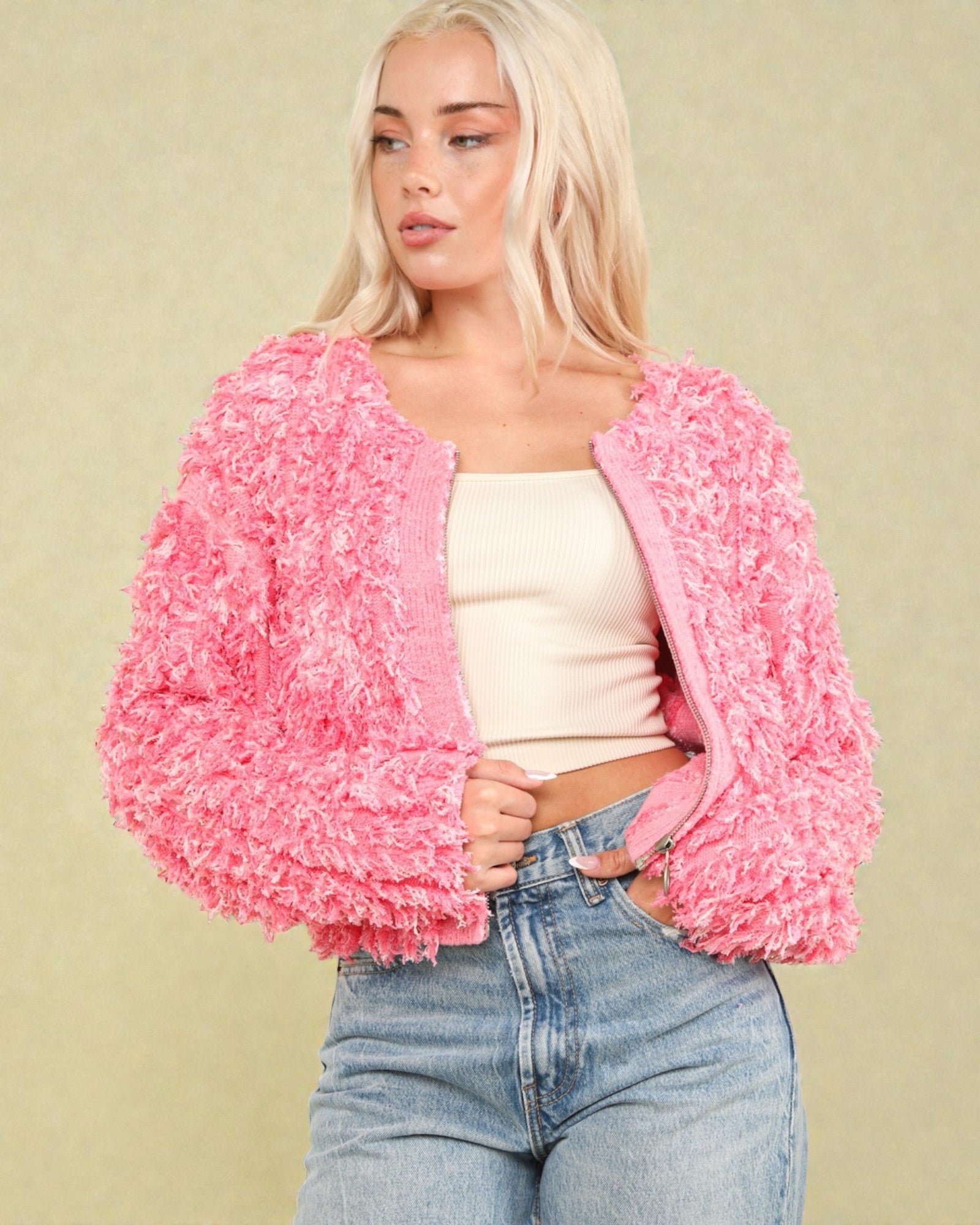 Woman wearing a pink textured jacket over a white top and blue jeans on a beige background