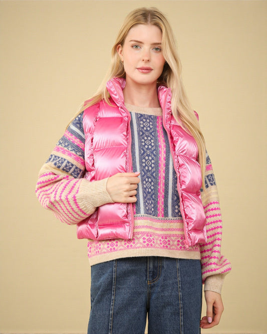 Woman wearing a pink puffer vest over a patterned sweater on a beige background