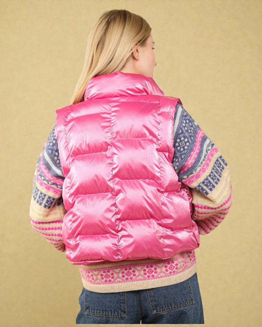 Person wearing a pink puffer vest over a patterned sweater on a beige background