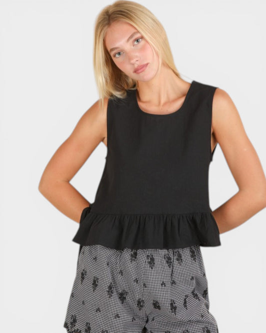 Woman wearing a black sleeveless top with ruffled hem on a white background