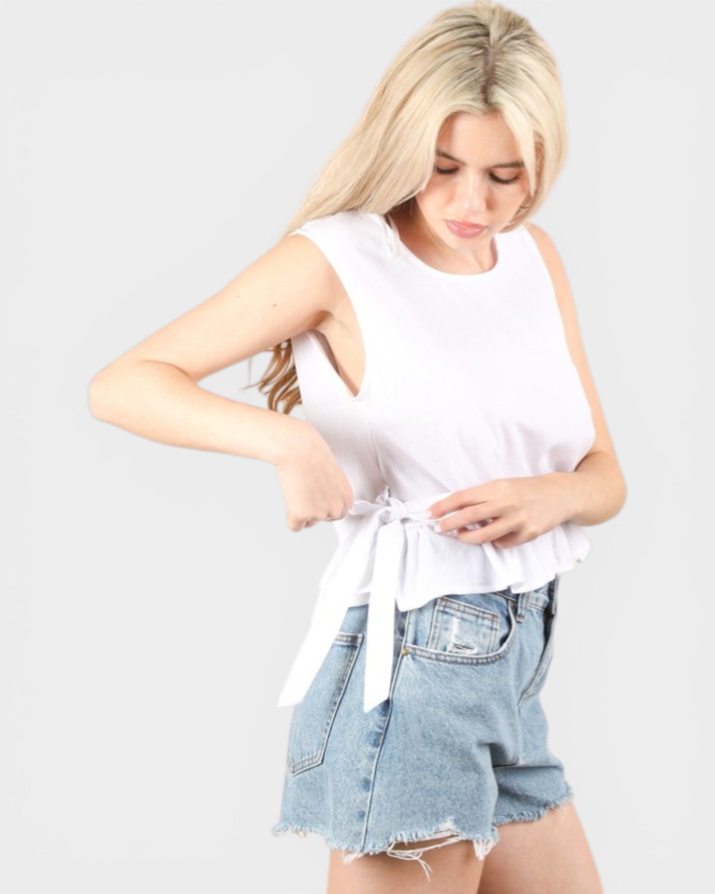 Woman wearing a white sleeveless top and denim shorts on a plain background