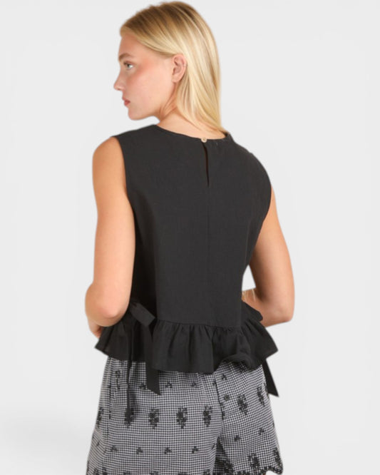 Woman wearing a black sleeveless top with ruffled details on a white background