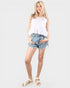 Woman wearing a white top and denim shorts on a plain background