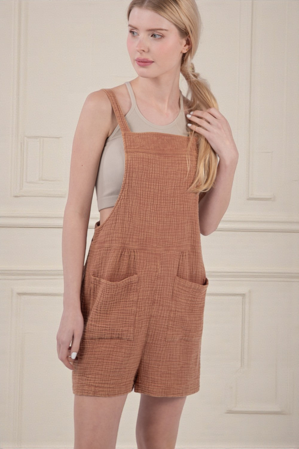 Woman wearing brown checkered overalls against a beige wall.