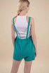 Woman wearing teal shorts with suspenders on a beige background
