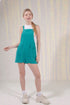 Woman wearing a teal pinafore dress against a neutral background