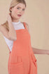 Woman wearing an orange checkered pinafore over a white top on a beige background