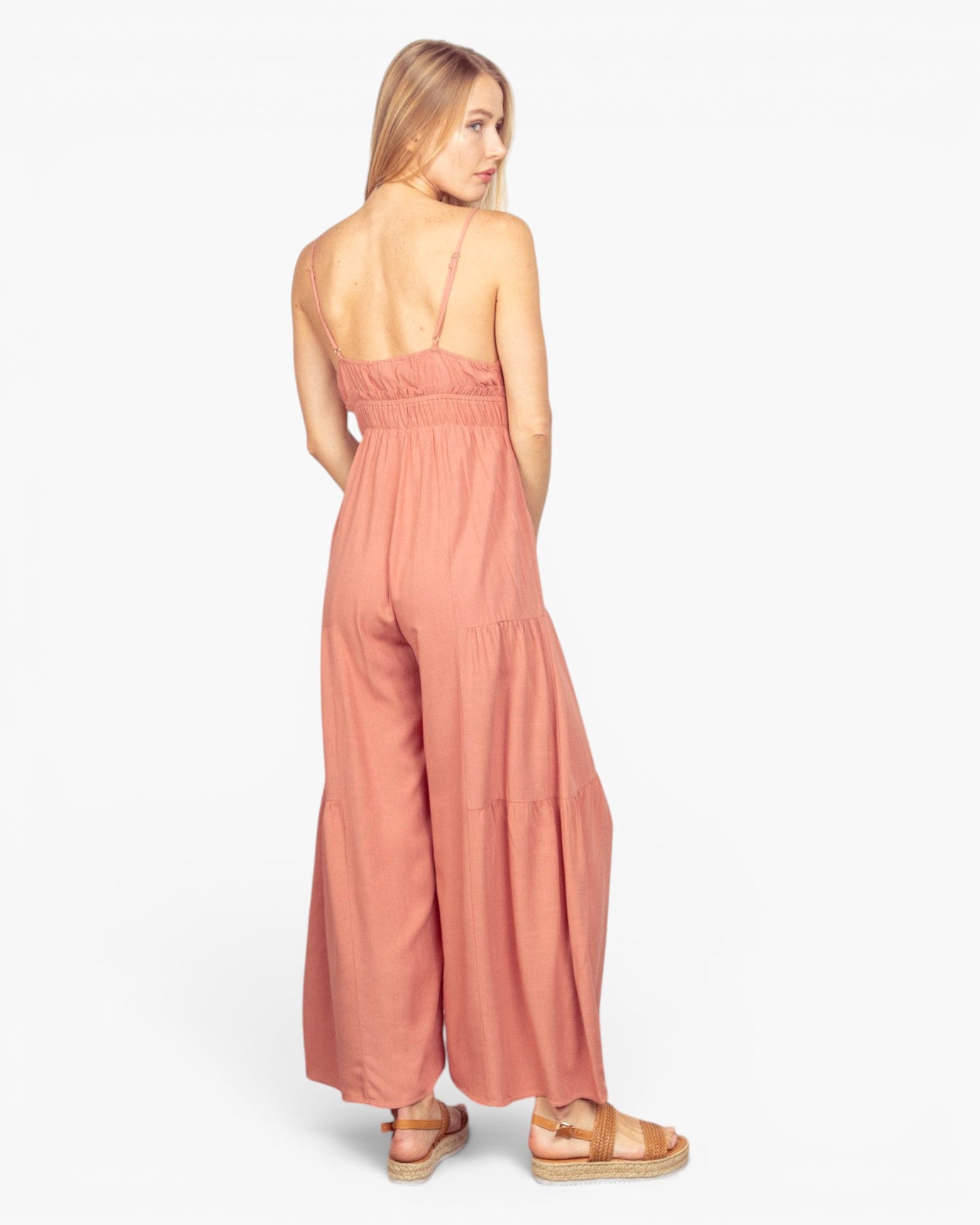 A woman wearing a dusty rose wide-leg jumpsuit, shown from the back against a plain white studio background.