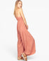 A woman modeling a dusty rose strapless maxi dress with a smocked waistband and tiered, wide-leg pants, paired with brown espadrille sandals against a plain white background.