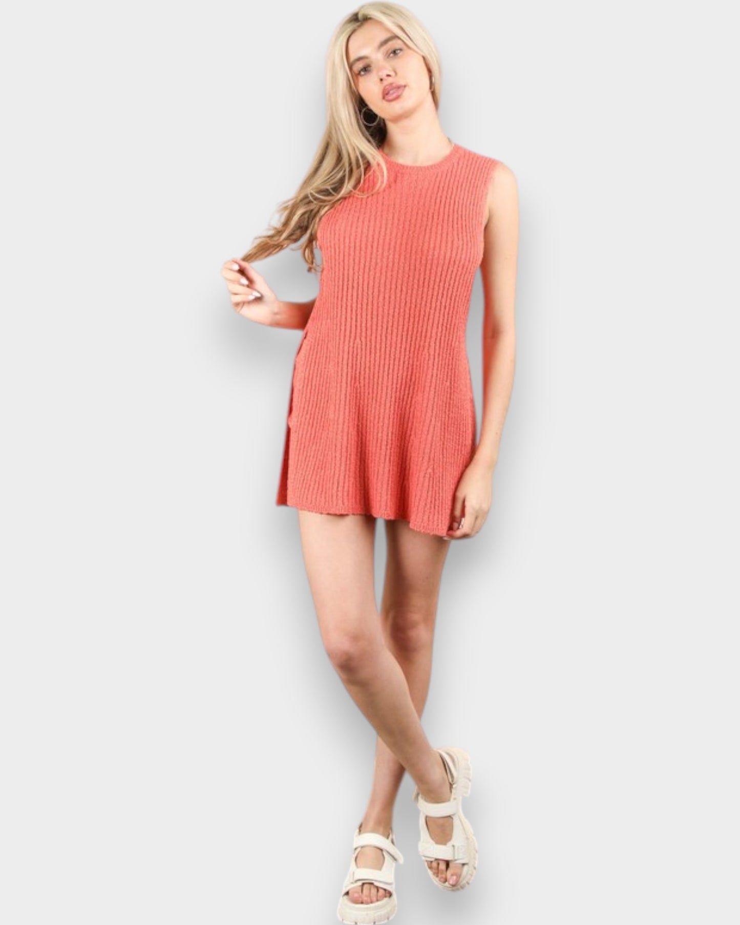 Woman wearing a coral sleeveless dress against a white background