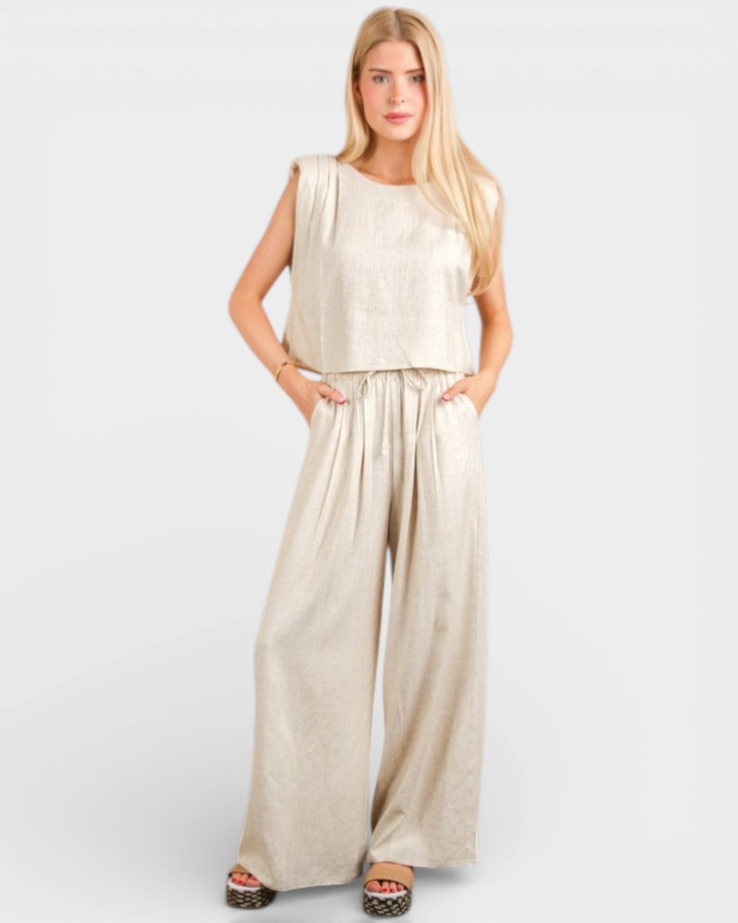 Woman wearing a beige sleeveless top and wide-leg pants on a white background