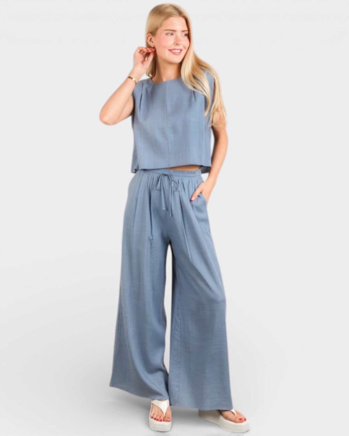 Woman wearing a blue sleeveless top and wide-leg pants on a white background