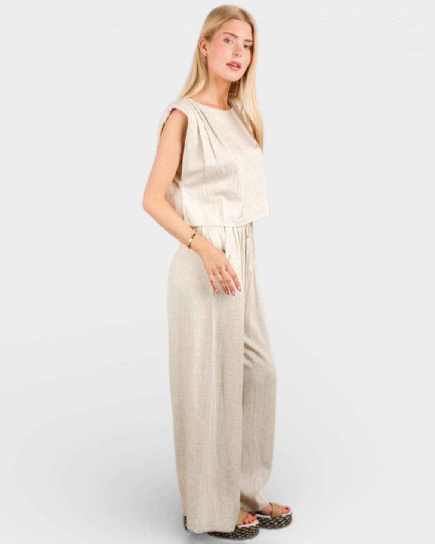 Woman wearing a beige sleeveless top and wide-leg pants on a white background