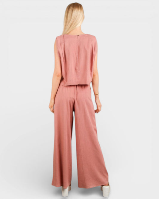 Woman wearing a pink sleeveless top and wide-leg pants on a white background