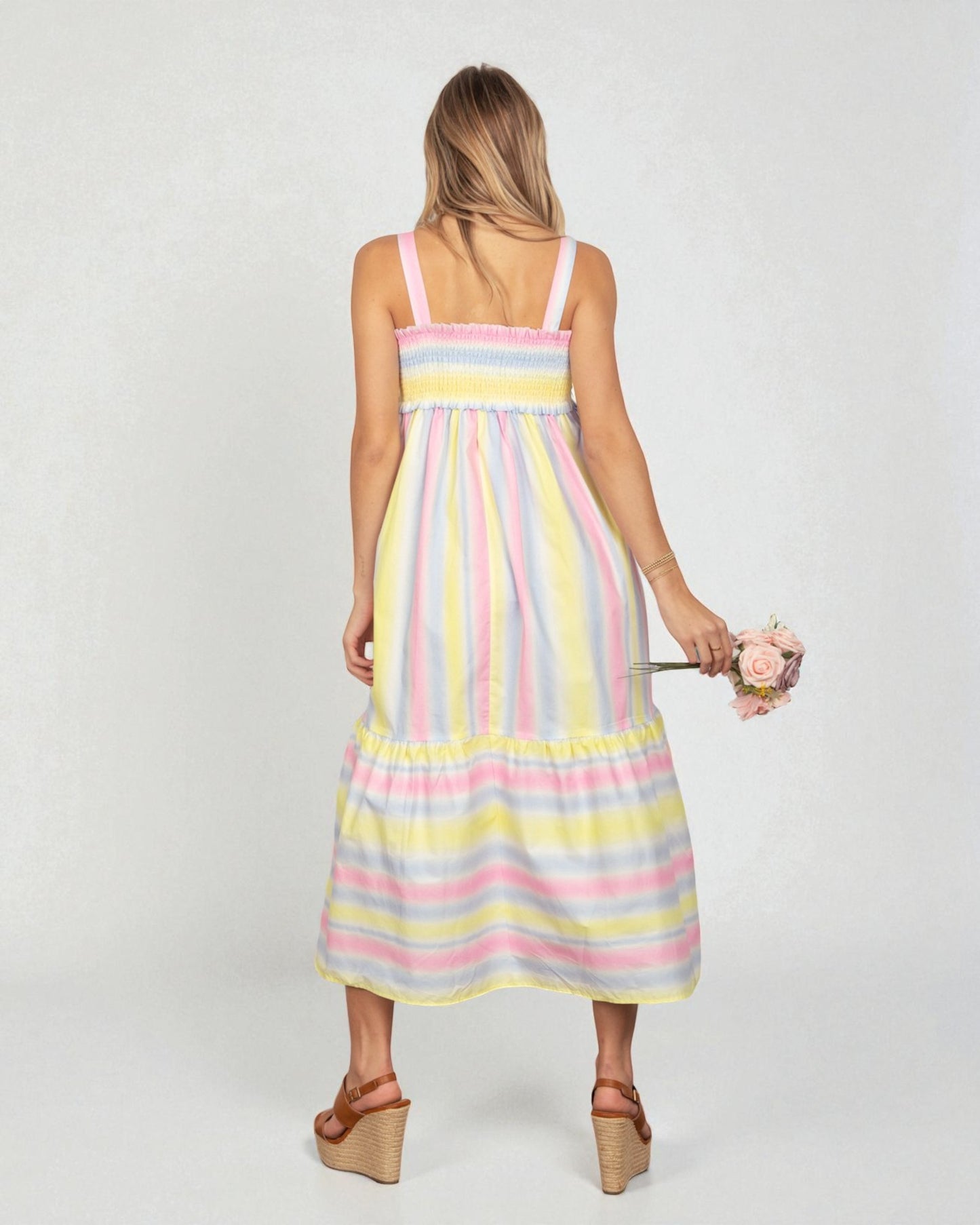 Woman wearing a pastel striped dress holding flowers on a white background