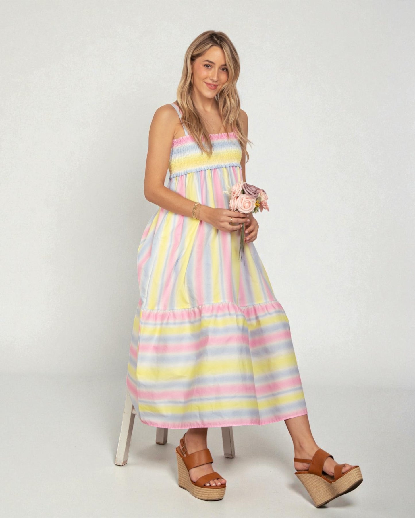 Woman wearing a pastel striped dress holding flowers on a white background