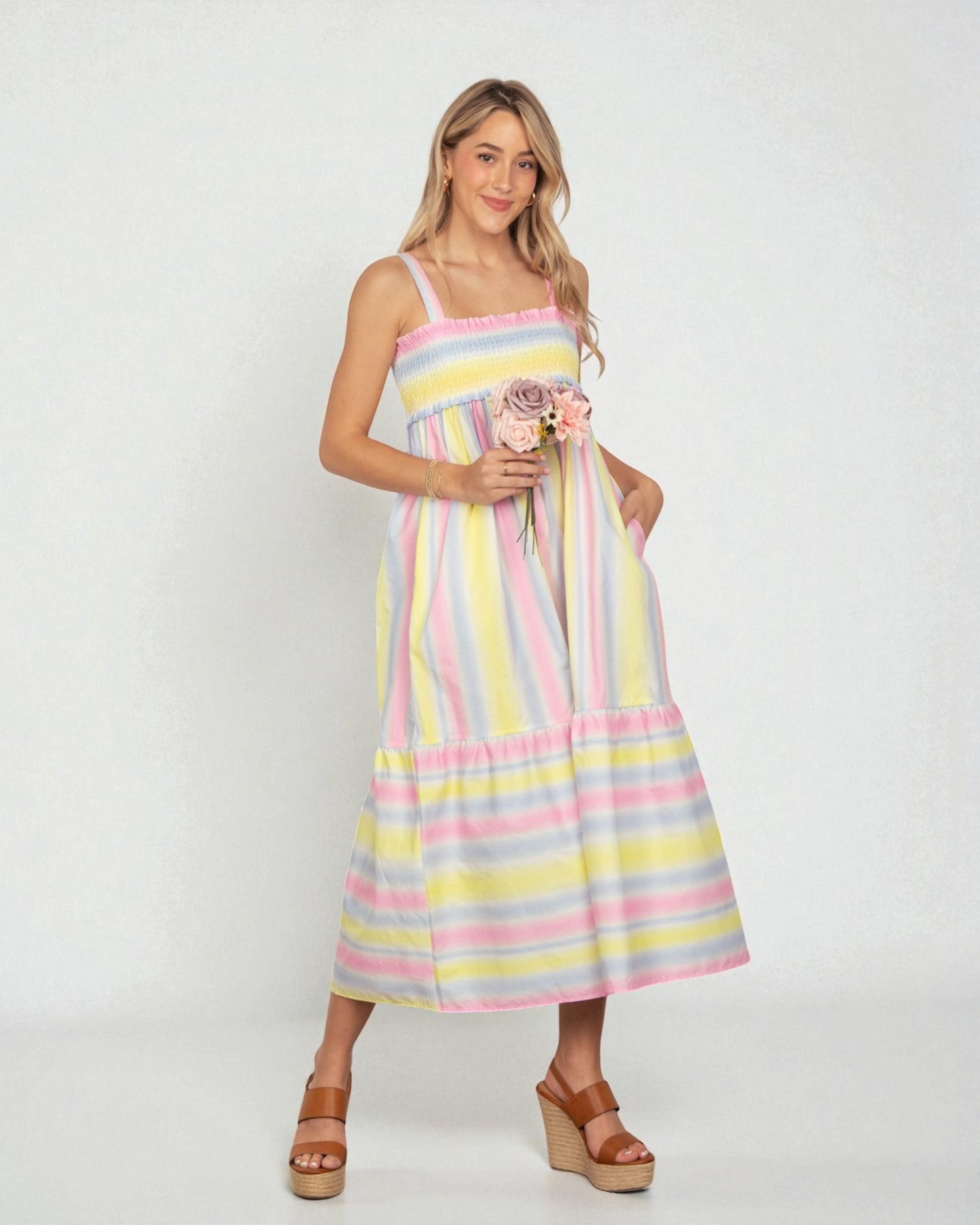 Woman wearing a colorful striped dress holding flowers against a white background