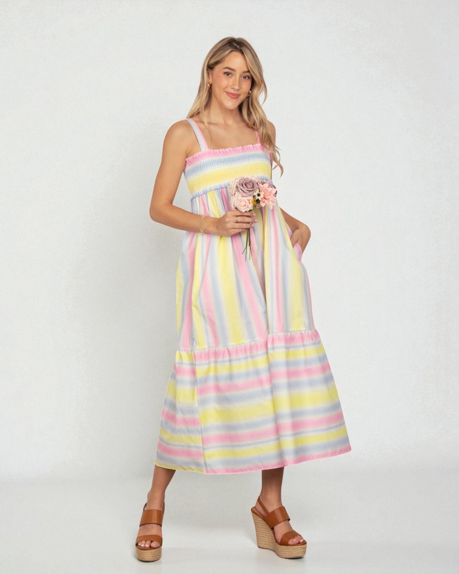Woman wearing a colorful striped dress holding flowers against a white background