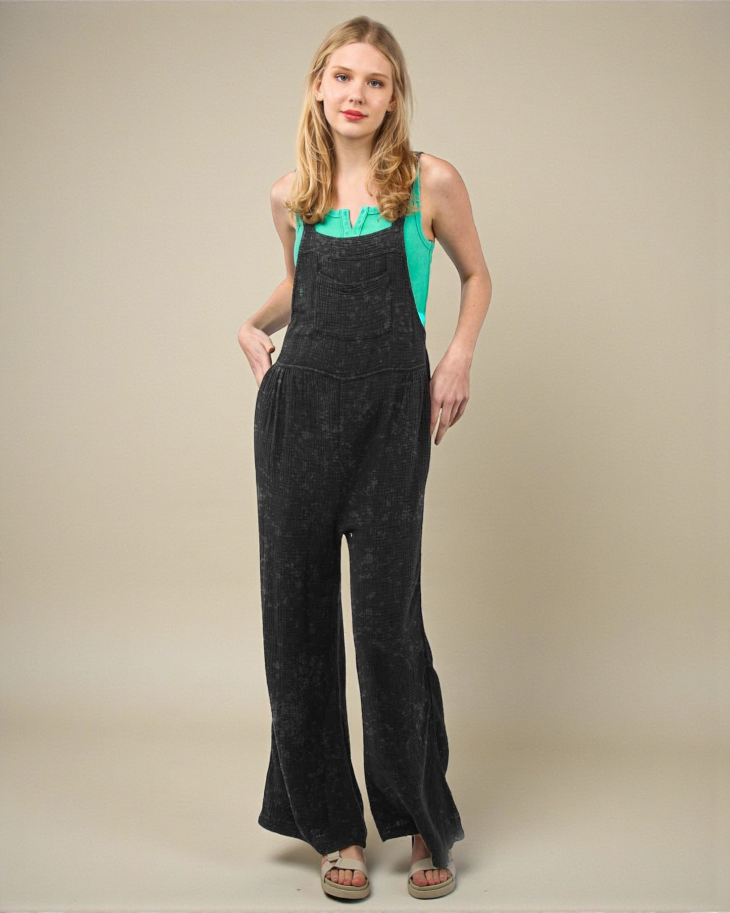 Woman wearing black overalls over a green top on a beige background