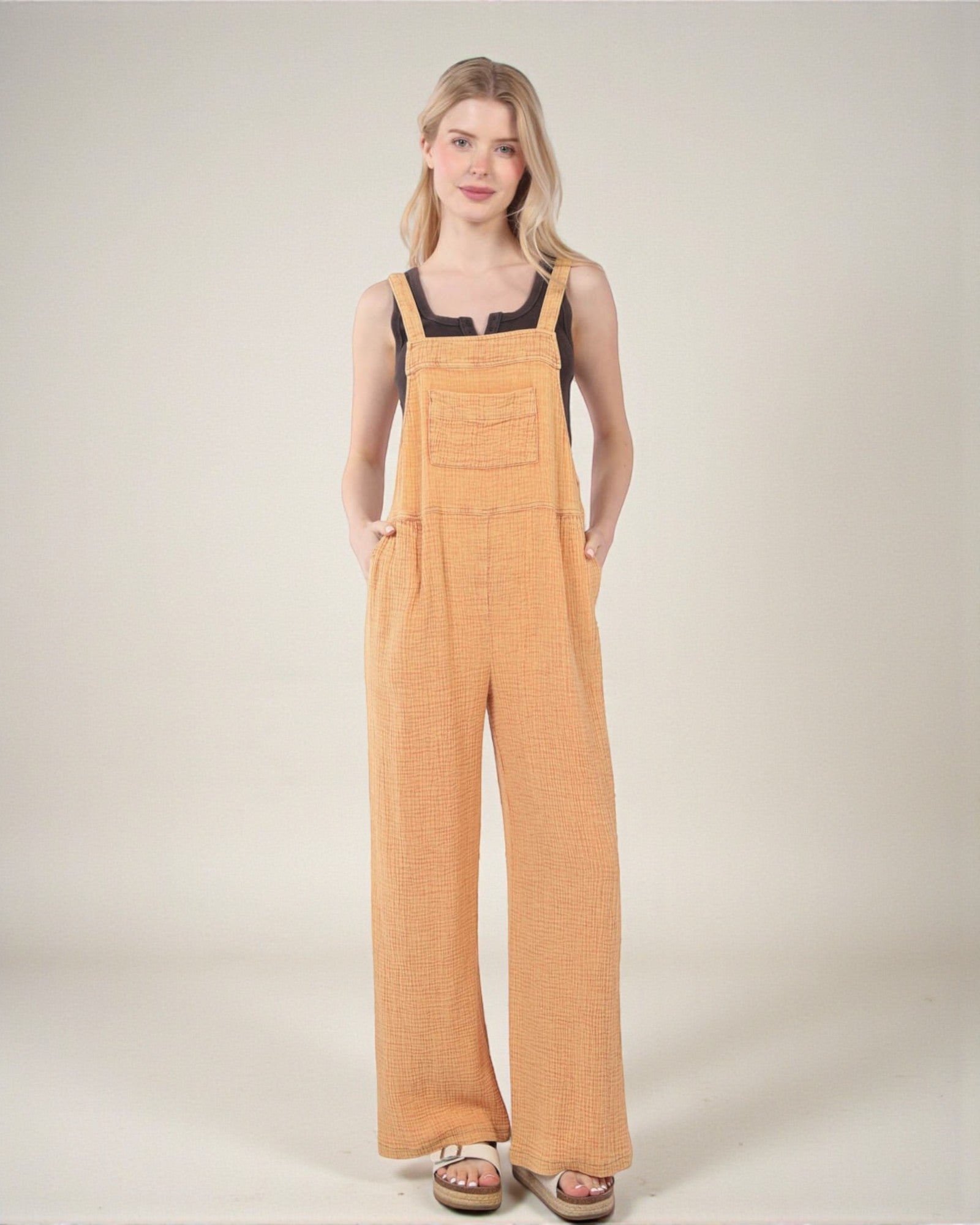 Woman wearing mustard yellow overalls on a plain background