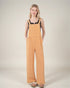 Woman wearing mustard yellow overalls on a plain background