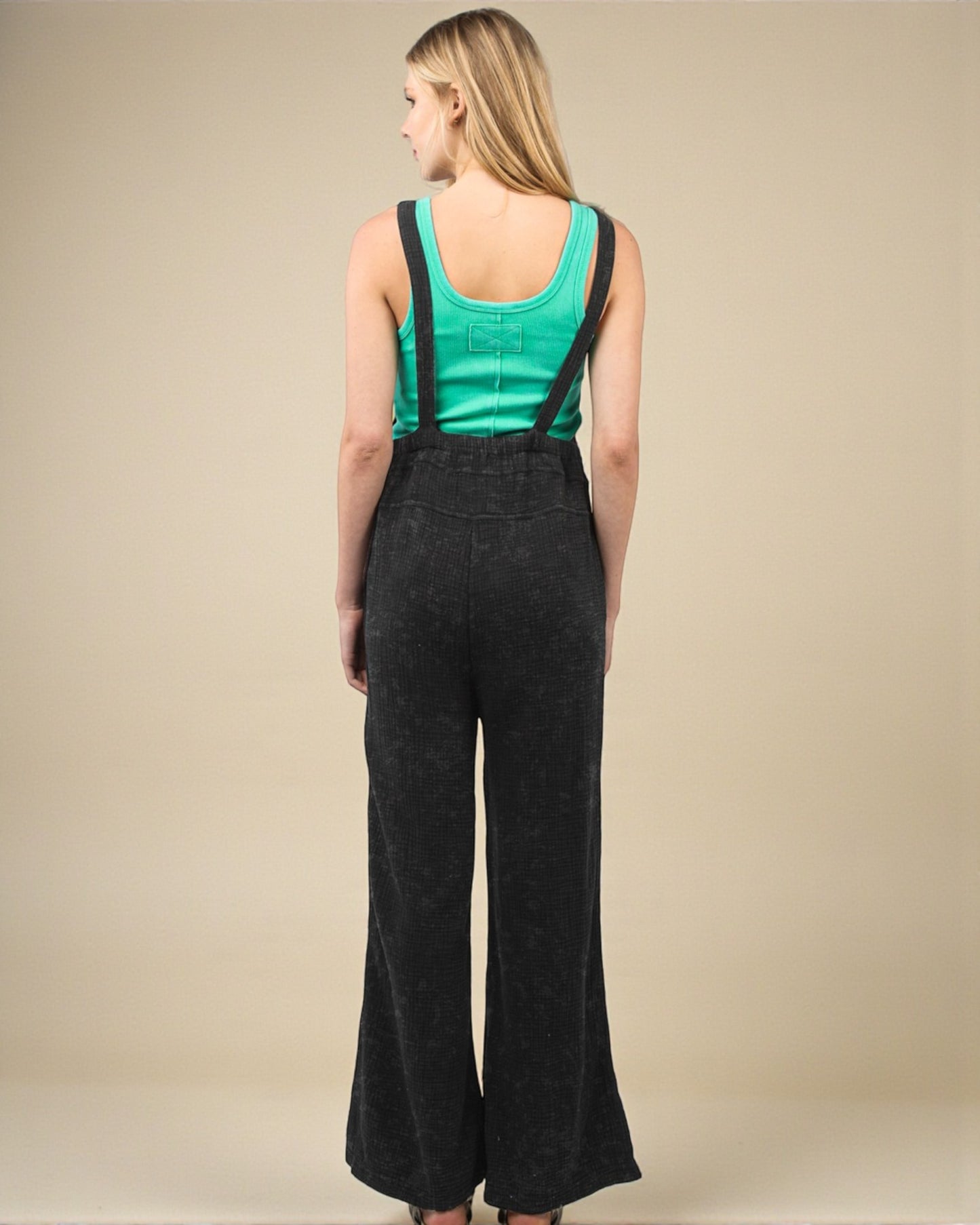 Woman wearing black overalls and a green tank top on a beige background
