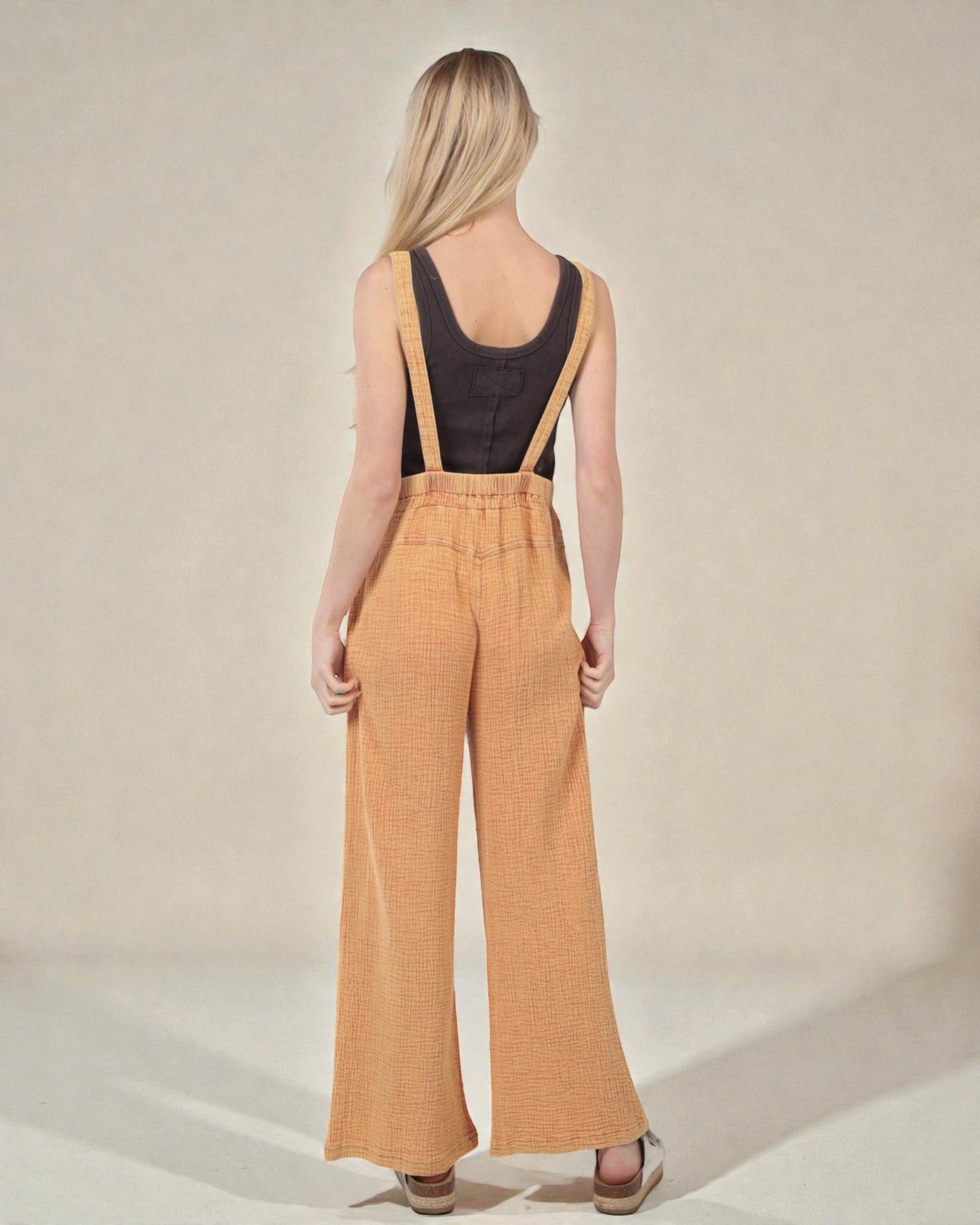 Woman wearing mustard yellow checkered overalls on a beige background