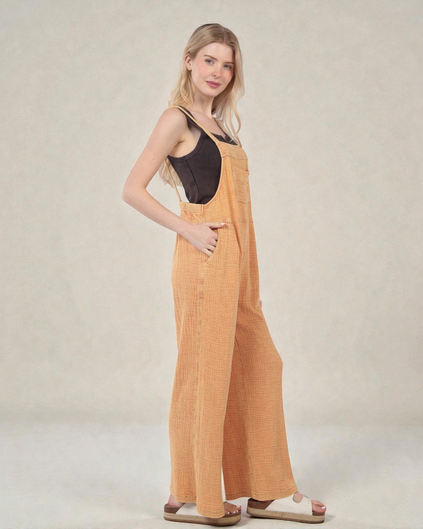 Woman wearing mustard yellow overalls against a plain background