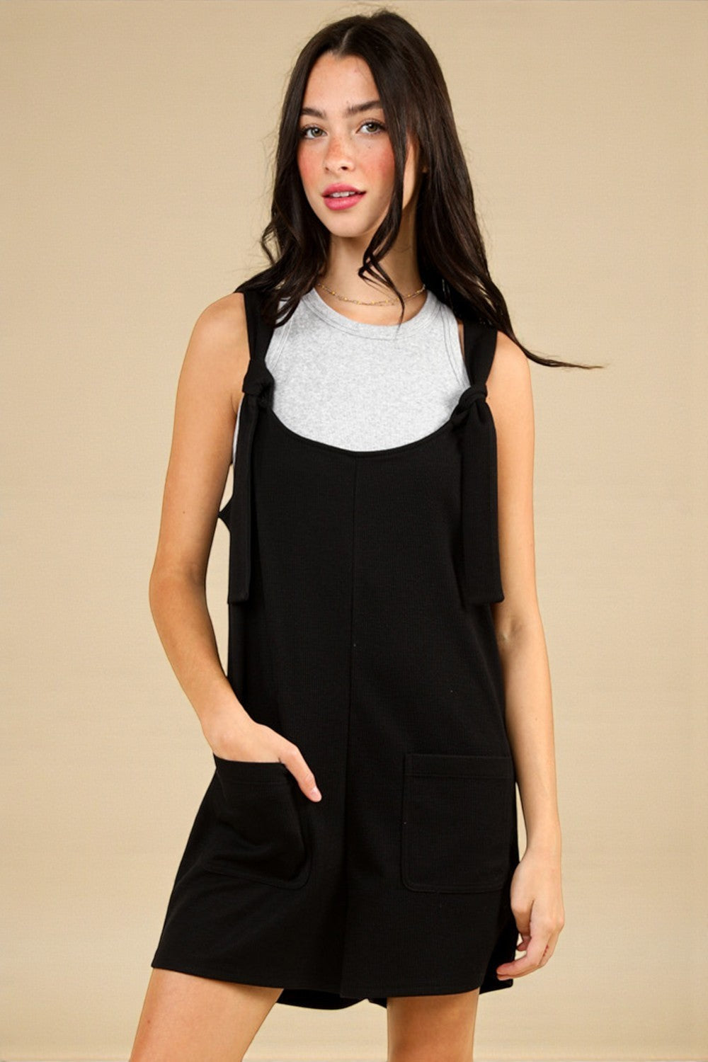 Woman wearing a black dress over a gray top against a beige background