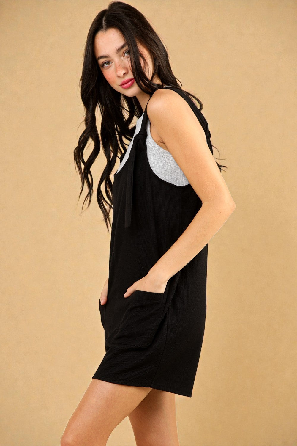 Woman wearing a black sleeveless dress with a beige background