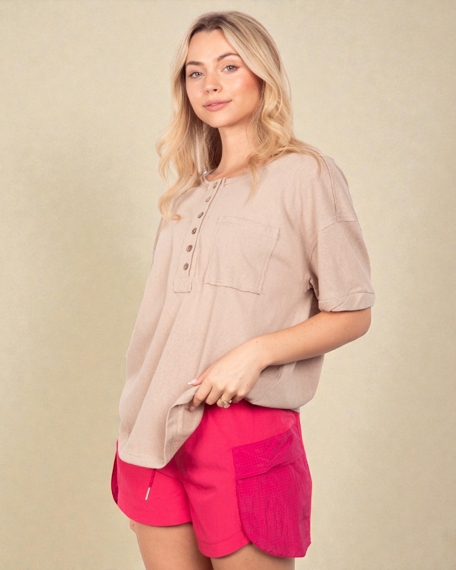 Woman wearing a beige shirt and pink shorts against a beige background