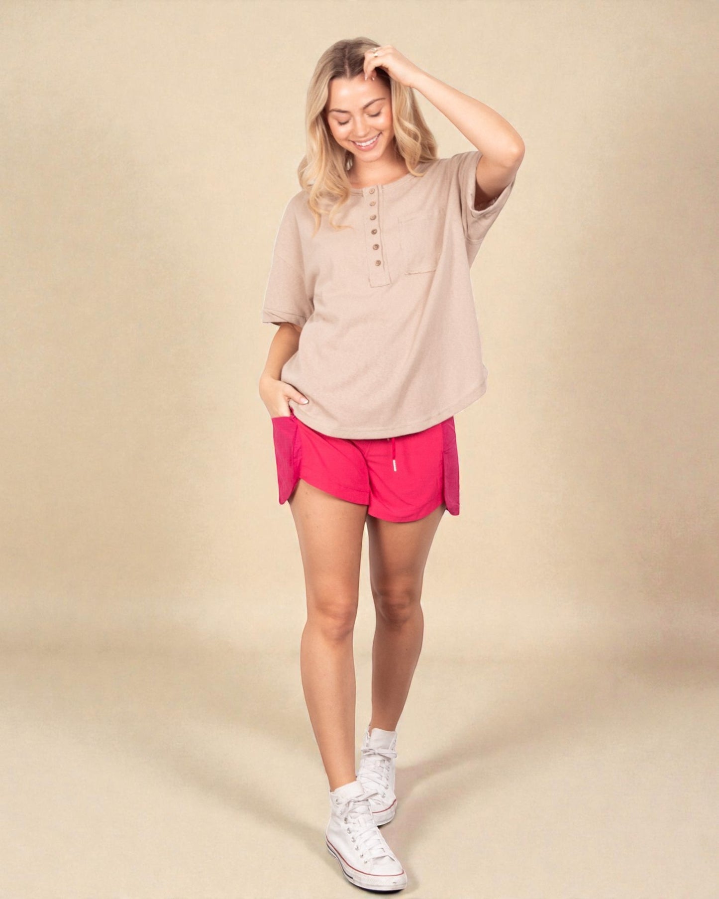 Woman wearing a beige shirt and pink shorts on a beige background