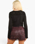 A woman shown from the back wearing a black long-sleeve ribbed knit top with lace shoulder panels and a dark burgundy fringed mini skirt, against a plain white background.