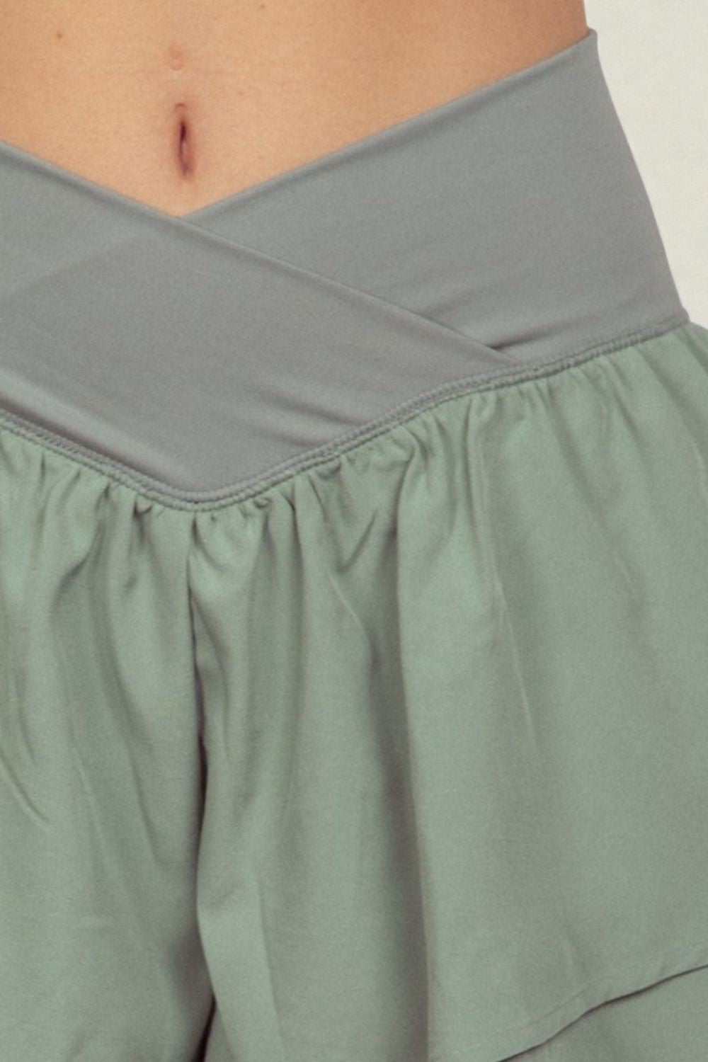 Close-up of a person wearing a gray top and green skirt against a white background