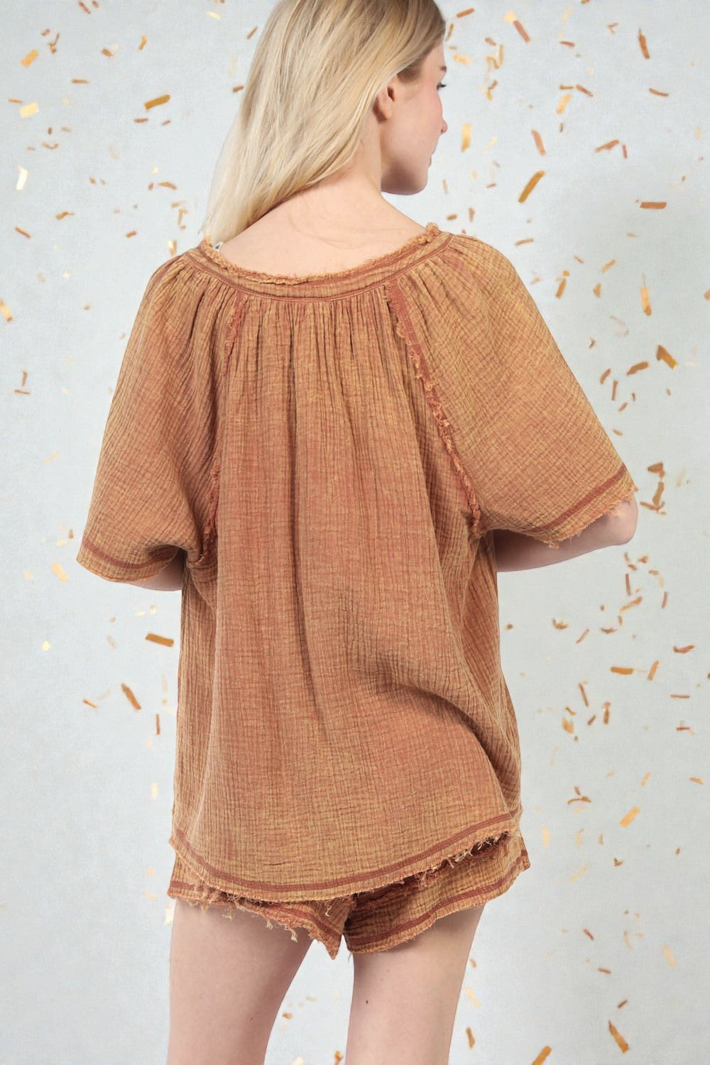 Woman wearing a brown textured top and shorts against a light background with confetti-like decorations.