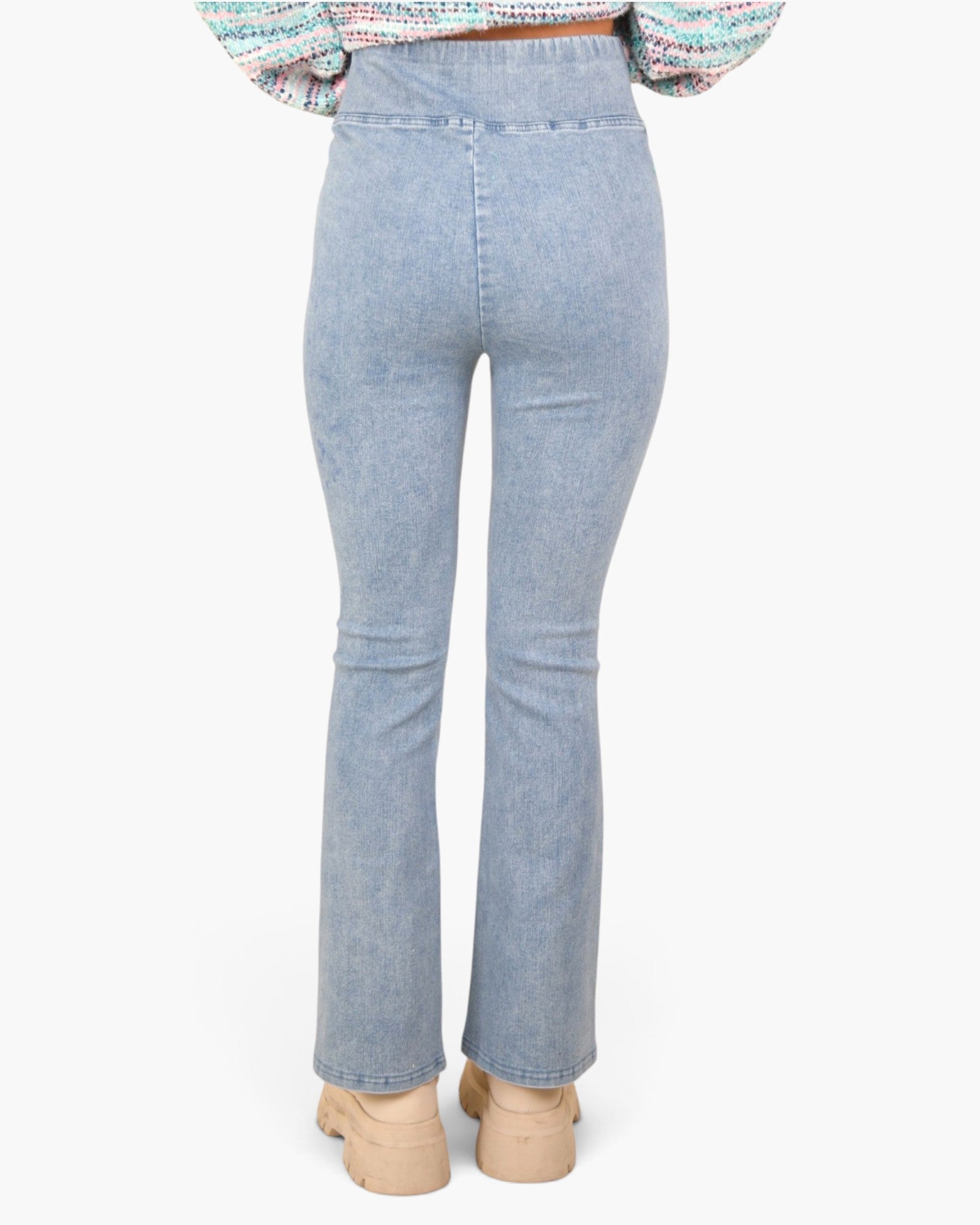 A person shown from the back wearing light-wash blue flared jeans, a multicolor knit top, and beige platform shoes against a plain light gray background.