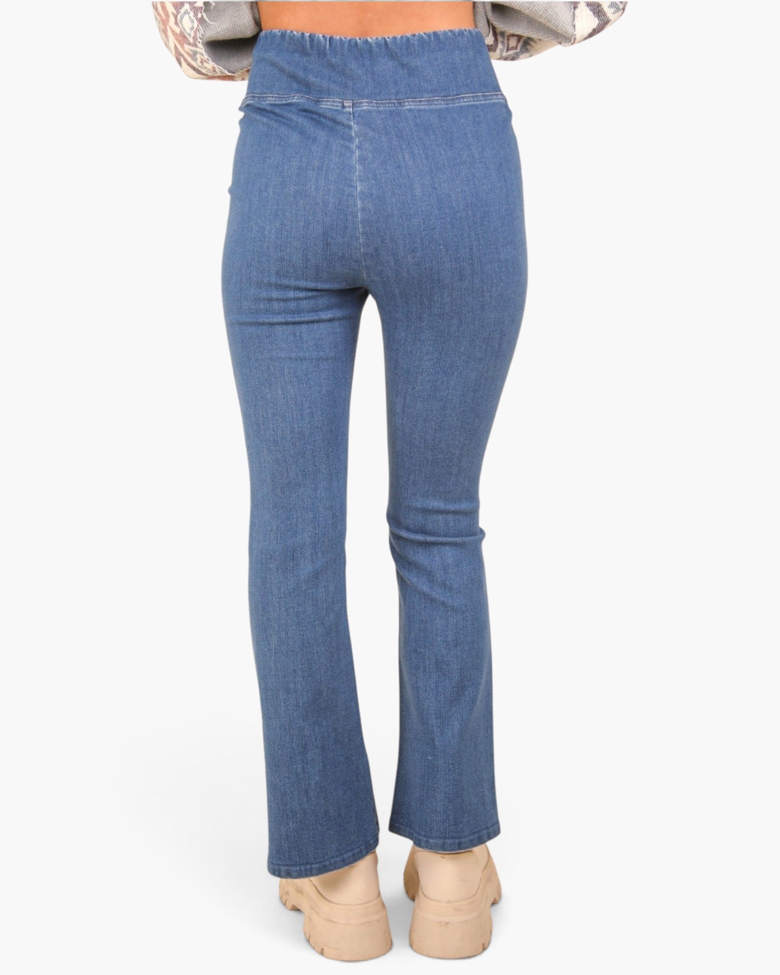 Rear view of a person wearing blue denim flare jeans with beige platform sandals against a plain light background.