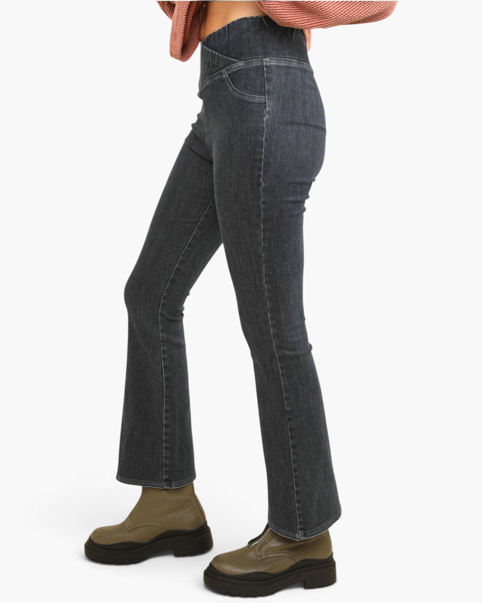 A person wearing dark gray flared denim jeans, olive green lace-up ankle boots, and a pink striped cropped sweater, shown from the waist down against a plain white background.