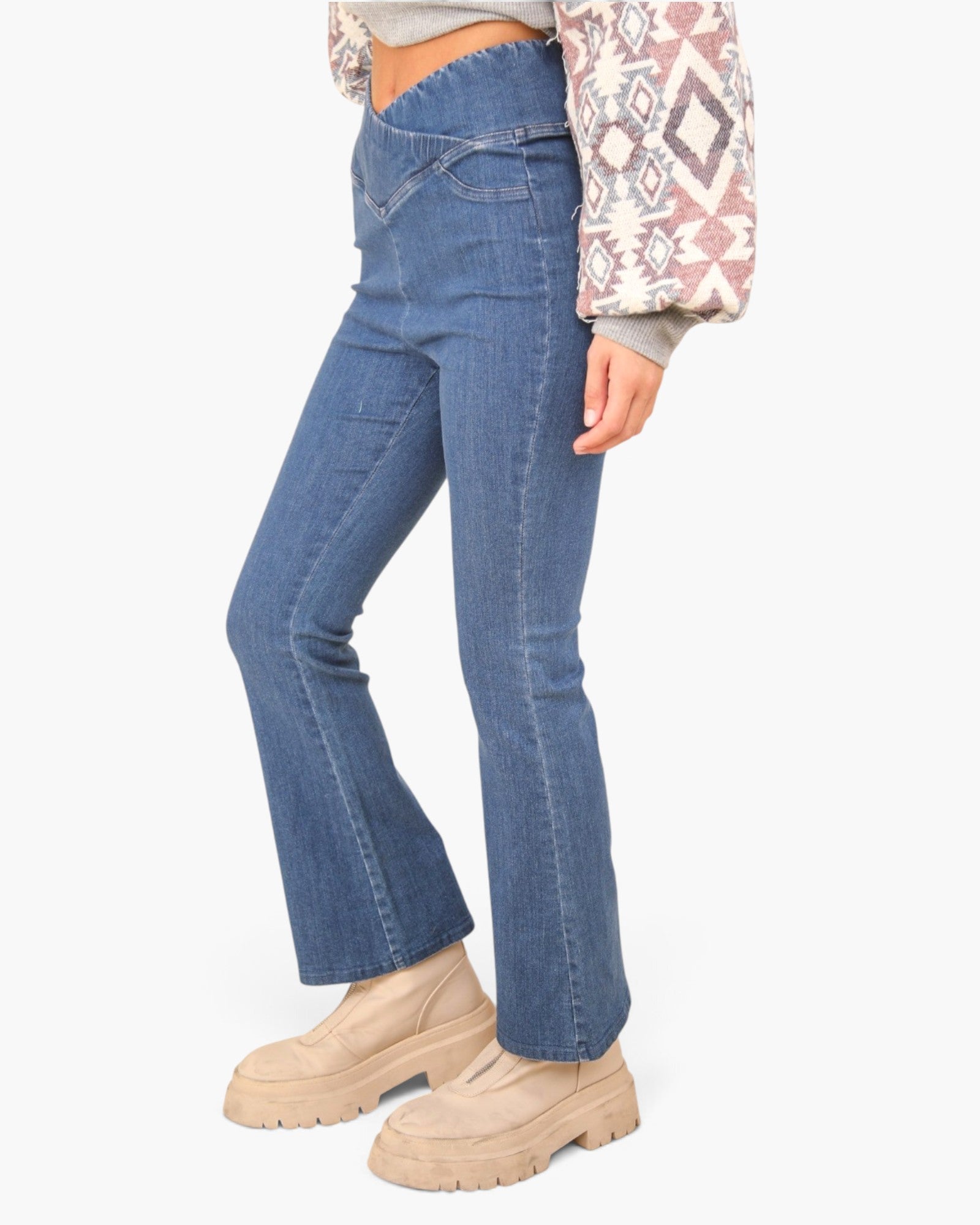 A person wearing medium-wash blue flare jeans with a high waist, paired with beige chunky platform shoes and a patterned long-sleeve top, shown against a plain light gray studio background.