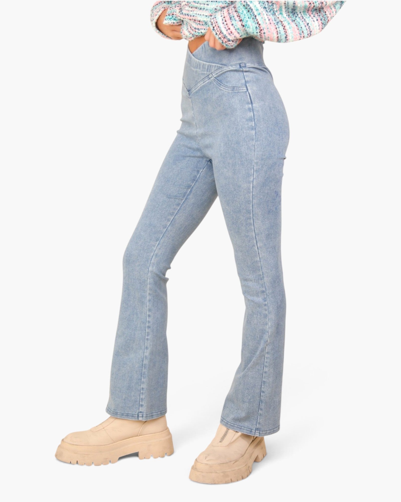 A model wearing light-wash blue high-rise flare jeans, paired with beige chunky platform boots and a multicolor knit top, shown from the waist down against a plain white background.
