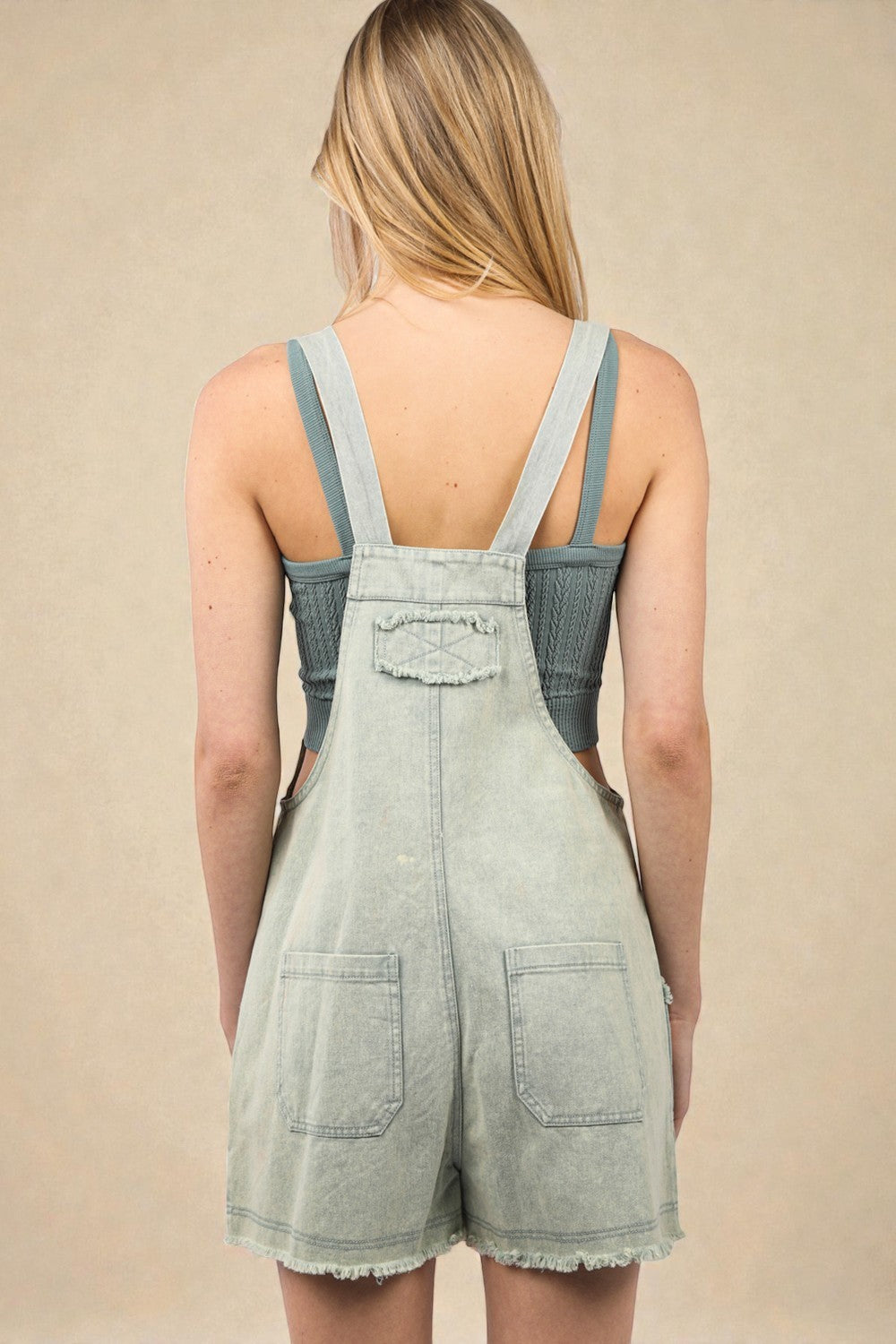 Light denim overalls worn by a person on a beige background