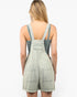 A woman shown from the back wearing a light sage green denim overall romper with frayed hems and wide shoulder straps, set against a plain white studio background.