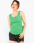 A woman wearing a bright green sleeveless henley tank top and dark brown shorts, standing against a plain white studio background.