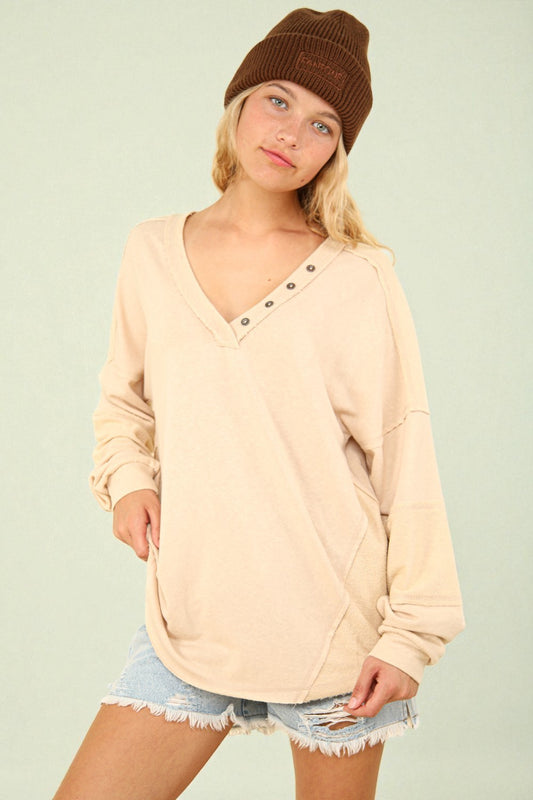 Woman wearing a beige long-sleeve top with button details, denim shorts, and a brown beanie on a light green background.