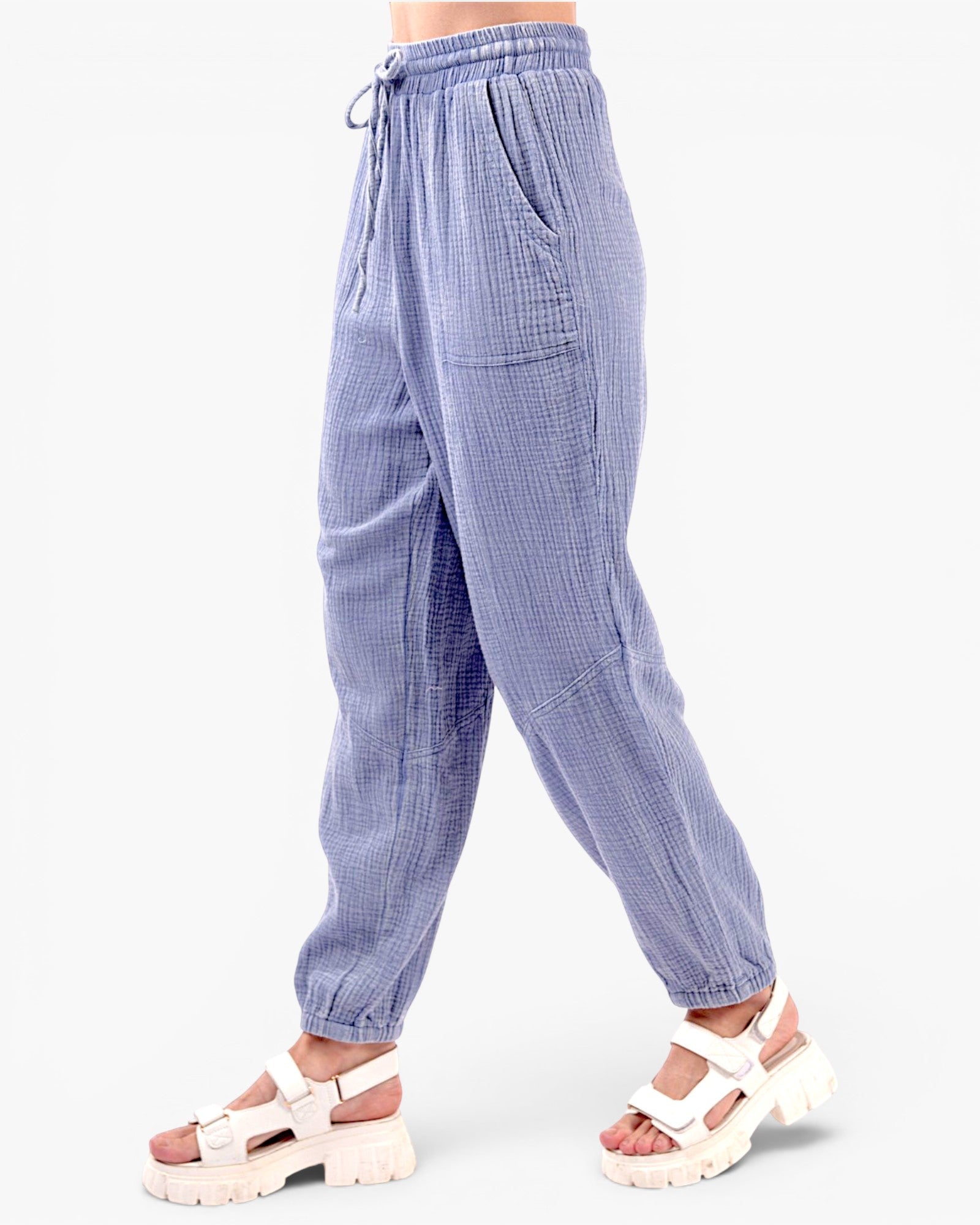 A person wearing loose, light blue-gray textured drawstring pants with side pockets and white platform sandals, shown from the waist down against a plain light background.