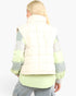 A woman shown from the back wearing a cream quilted puffer vest over a light green and gray color-blocked long-sleeve shirt, paired with gray pants, against a plain white background.