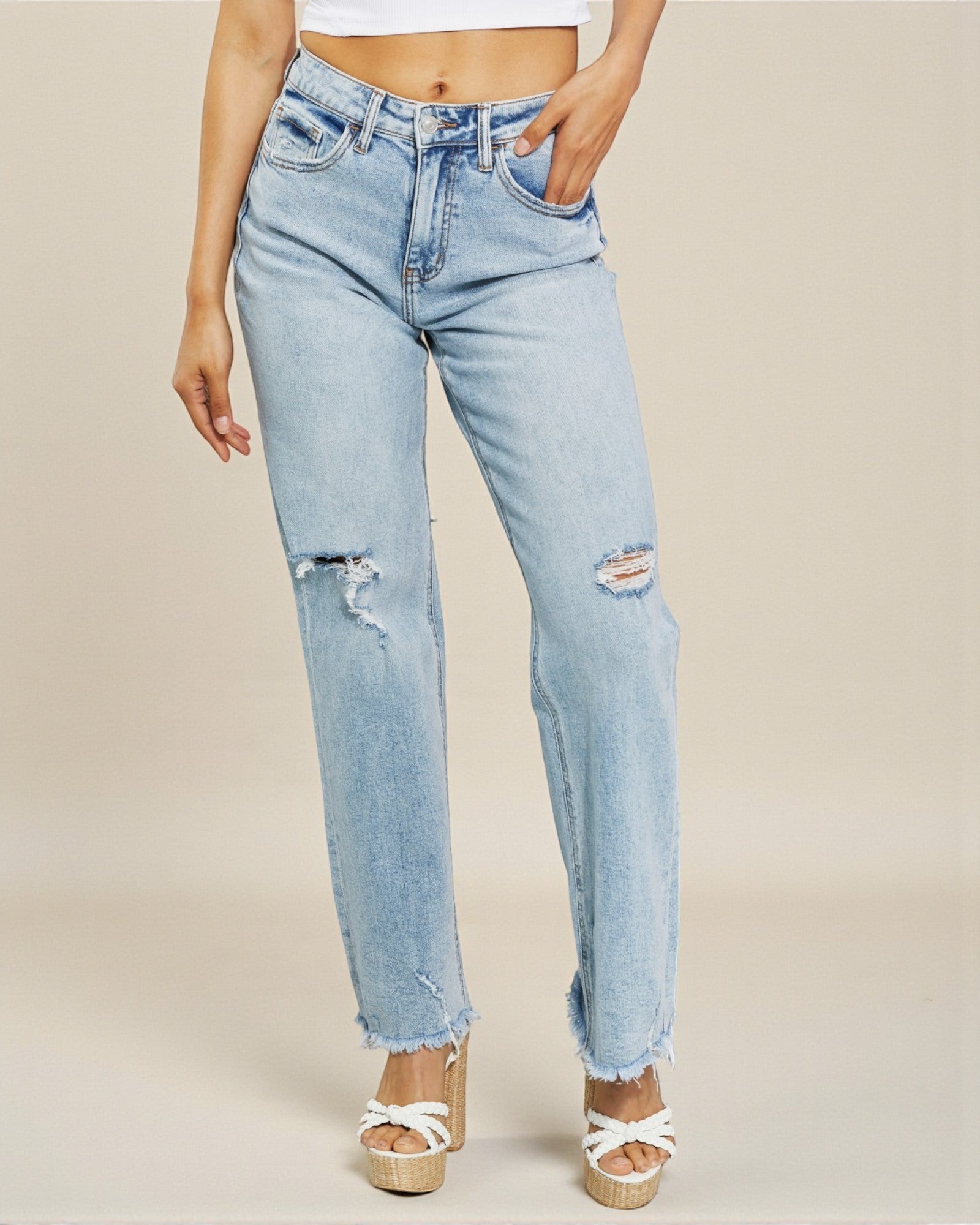 Light blue jeans with distressed details worn by a person on a beige background